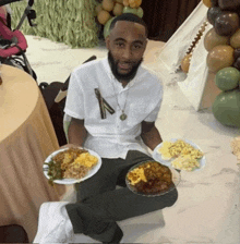 a man sitting on the floor holding plates of food