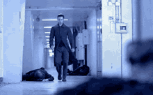 a man in a trench coat walks down a hallway with a man laying on the floor