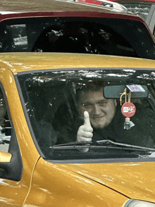 a man giving a thumbs up while sitting in a car with a sticker on the rear view mirror that says 24