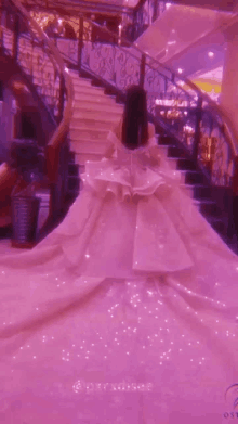 a girl in a long pink dress is standing on a set of stairs .