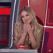 a woman in a gold sequined dress is sitting in a chair with a red button that says the voice on it