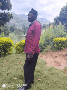 a man in a red shirt is standing in a grassy area with a ditel s18 4g phone in the background