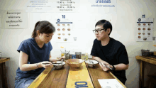 a man and a woman sit at a table with bowls of food in front of a sign that says 10 and 11