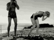 a black and white photo of a man and a woman on the beach with the caption " i got water in my ear "