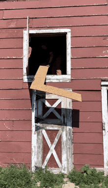 a red building with a broken window and a piece of wood in front of it