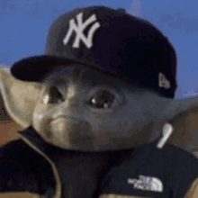 the baby yoda is wearing a new york yankees hat and a north face jacket .