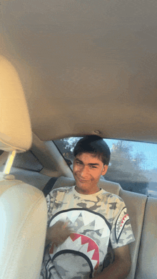 a young man wearing a shark t-shirt is sitting in the back seat of a car