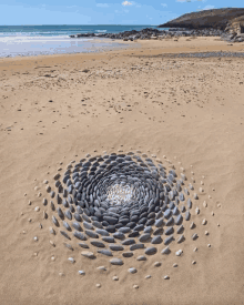 a circular pattern of rocks on a sandy beach with the ocean in the background