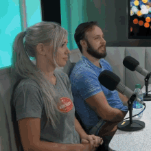 a man and a woman are sitting in front of microphones and the woman is wearing a t-shirt that says awesome