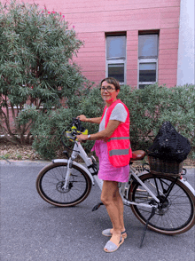 a woman wearing a pink vest is standing next to a bicycle