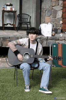 a man sitting in a chair holding a guitar with the letters bts on the bottom