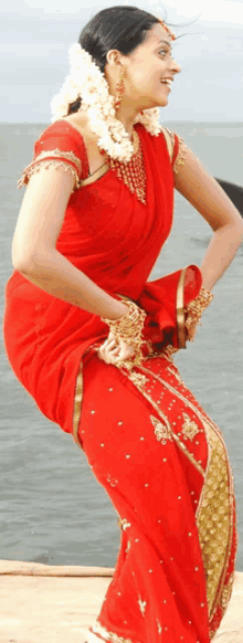 a woman in a red and gold dress is dancing in front of the ocean