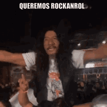 a man with long hair and a mustache is dancing in front of a crowd with the words " queremos rockanrol " above him