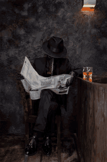 a man in a black suit reads a newspaper while sitting at a bar