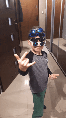 a young boy wearing sunglasses and a gray shirt is giving the peace sign