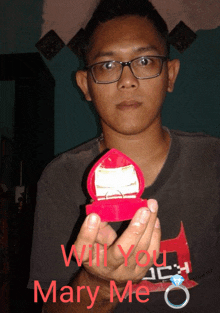 a man wearing glasses is holding a heart shaped box with a ring inside of it