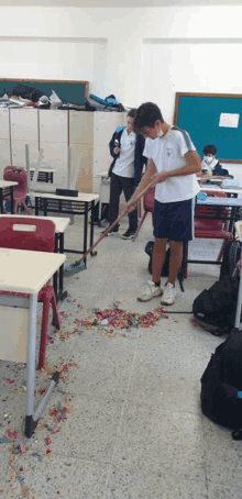 a boy wearing a mask is sweeping the floor of a classroom with a broom