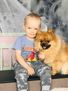 a little boy wearing a marvel t-shirt sits next to a small dog