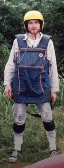 a man wearing a yellow helmet and overalls stands in the grass