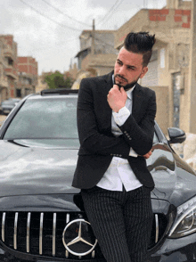 a man in a suit leans against a mercedes car