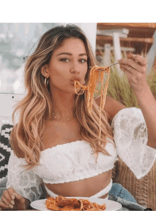 a woman in a white top is eating spaghetti