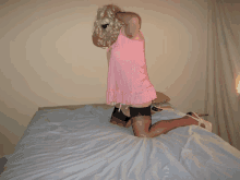 a woman in a pink dress is kneeling down on a bed