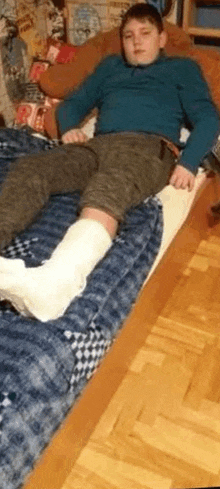 a young man is laying on a bed with a cast on his leg .