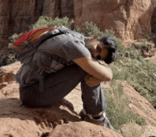 a man with a backpack is kneeling on a rock