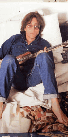 a man is sitting on a bed playing a guitar