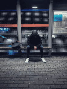 a man sits on a bench at a bus stop with a sign that says sleep on it