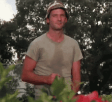 a man wearing a hat and a t-shirt is standing in front of a garden .