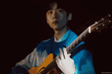 a man in a blue sweater is playing a guitar in a dark room