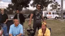 a group of people are sitting in chairs in a park while a man stands in front of an ice cream truck .