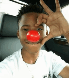 a young boy is wearing a red clown nose while sitting in a car .