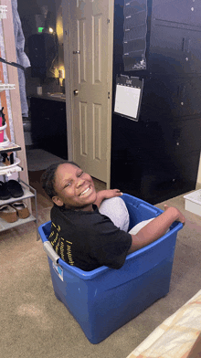 a girl in a black shirt is sitting in a blue plastic bin