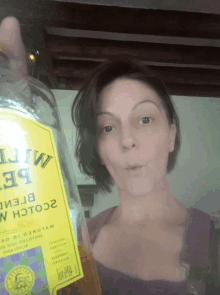 a woman is holding up a bottle of tequila with a yellow label