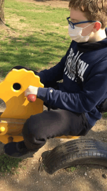 a boy wearing a mask and a champion sweatshirt is playing on a rocking horse