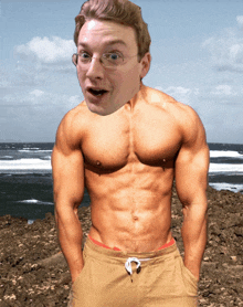 a shirtless man with glasses stands on a rocky beach