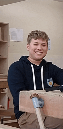 a young man in a blue hoodie is smiling in a classroom with a sign on the wall that says " lotto "