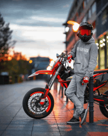 a man leaning against a pole next to a red dirt bike with a hoodie that says fox