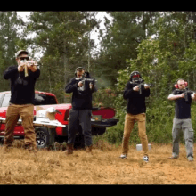 a group of men are standing in a field holding guns in front of a red truck