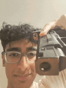 a young man wearing glasses holds a gun up to his face