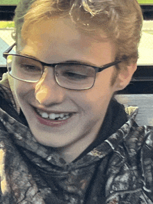 a young man wearing glasses and a camo sweatshirt smiles