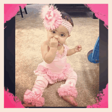 a baby girl wearing a pink outfit and headband biting her thumb