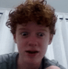 a young man with red curly hair is making a funny face while looking at the camera .