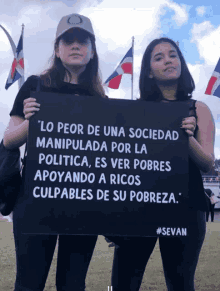 two women holding a black sign that says " lo peor de una sociedad manipulada por la politica "