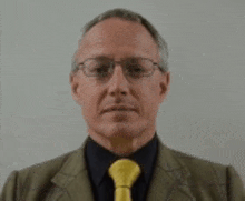 a man wearing glasses and a yellow tie looks at the camera .