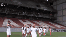 a group of soccer players are on a field in front of a stadium that has a large a on it