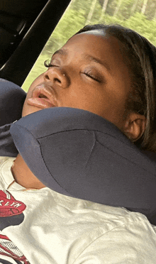 a young girl is sleeping in a car with a pillow around her neck