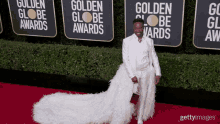 a man in a white suit is standing on a red carpet in front of signs that say golden globe awards